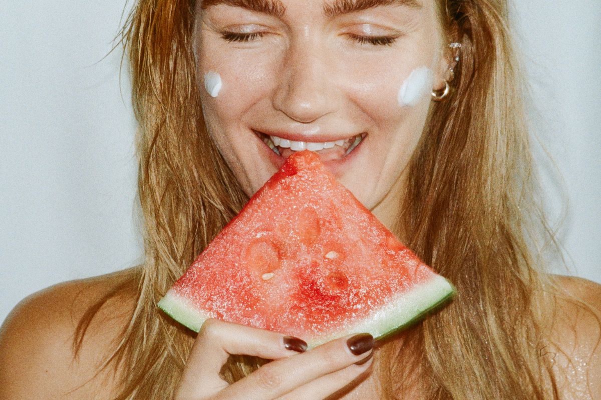 Mergina valganti arbūzą su saulės kremu